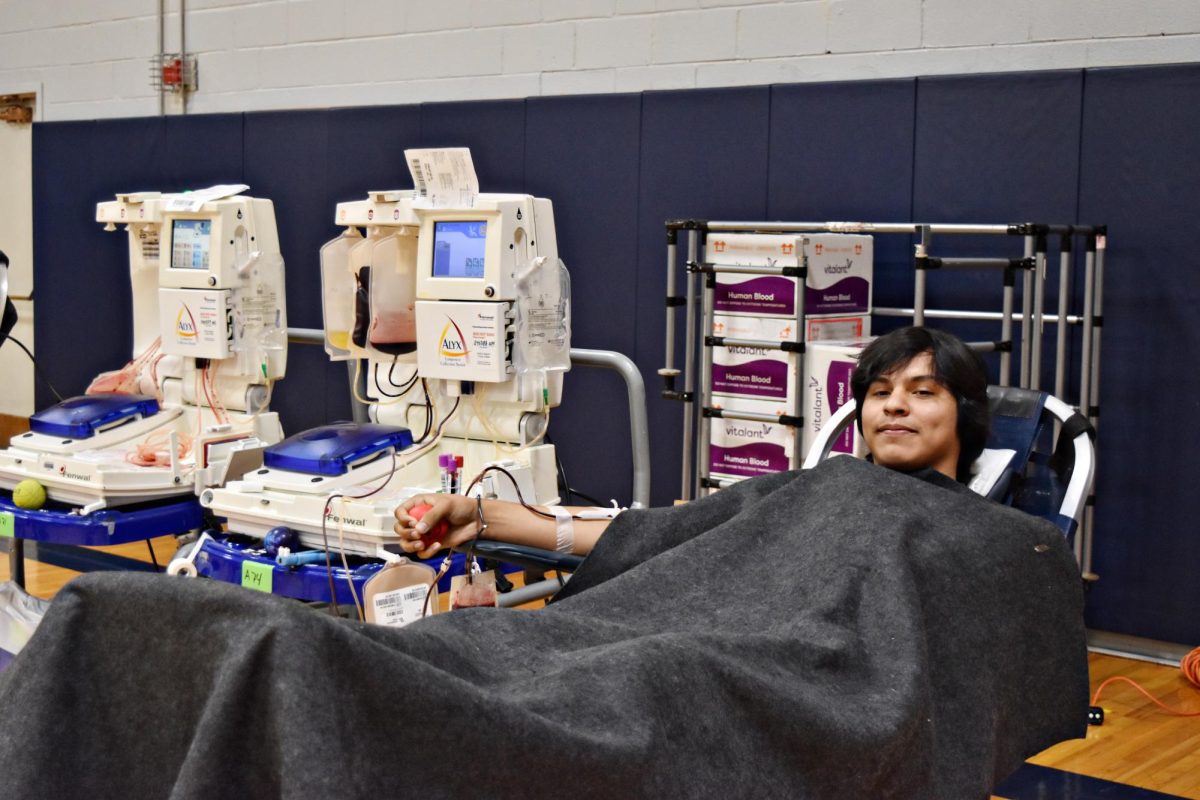 Junior Edgar Oropeza stays warm under a blanket as he donates blood in the gym on Oct. 13, 2023.