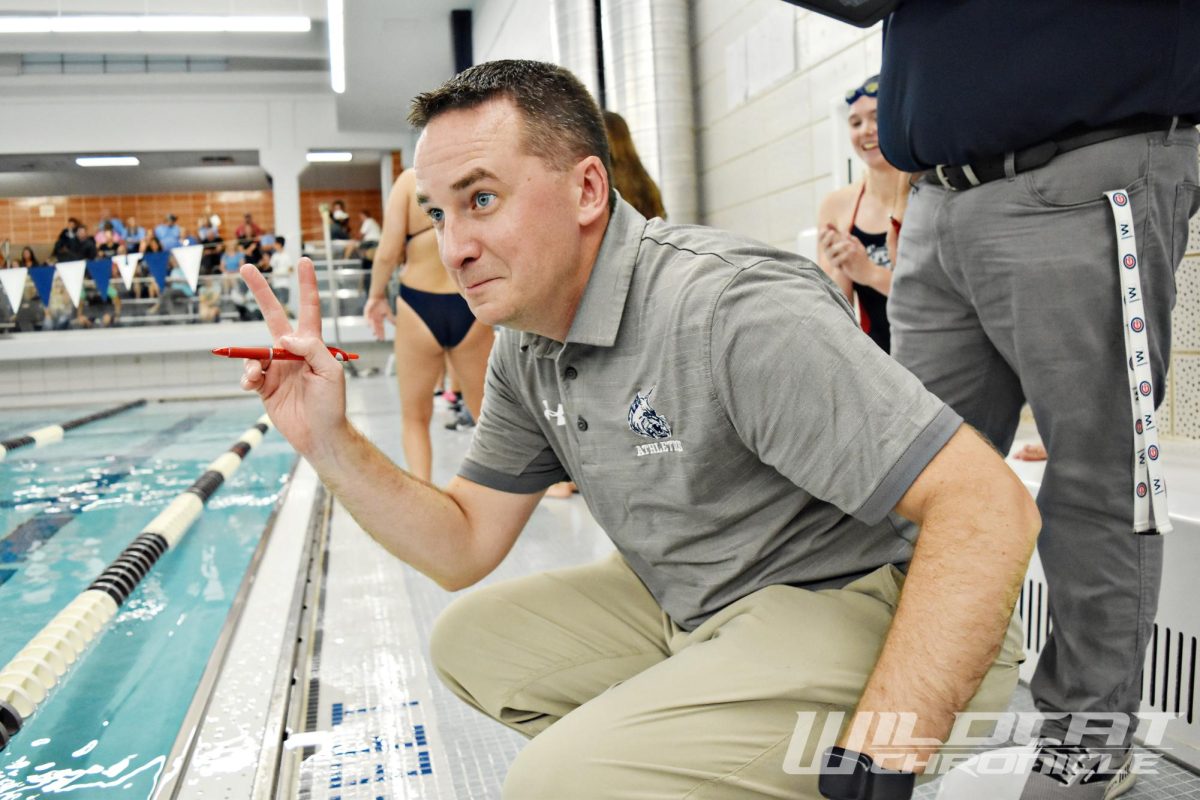 Girls swim coach Nick Parry indicates how many laps one of his swimmers has left to go on her race.
