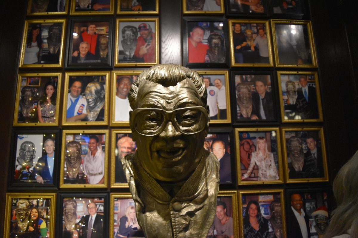 A statue of Harry Caray in front of many photos of celebrities standing with the statue.