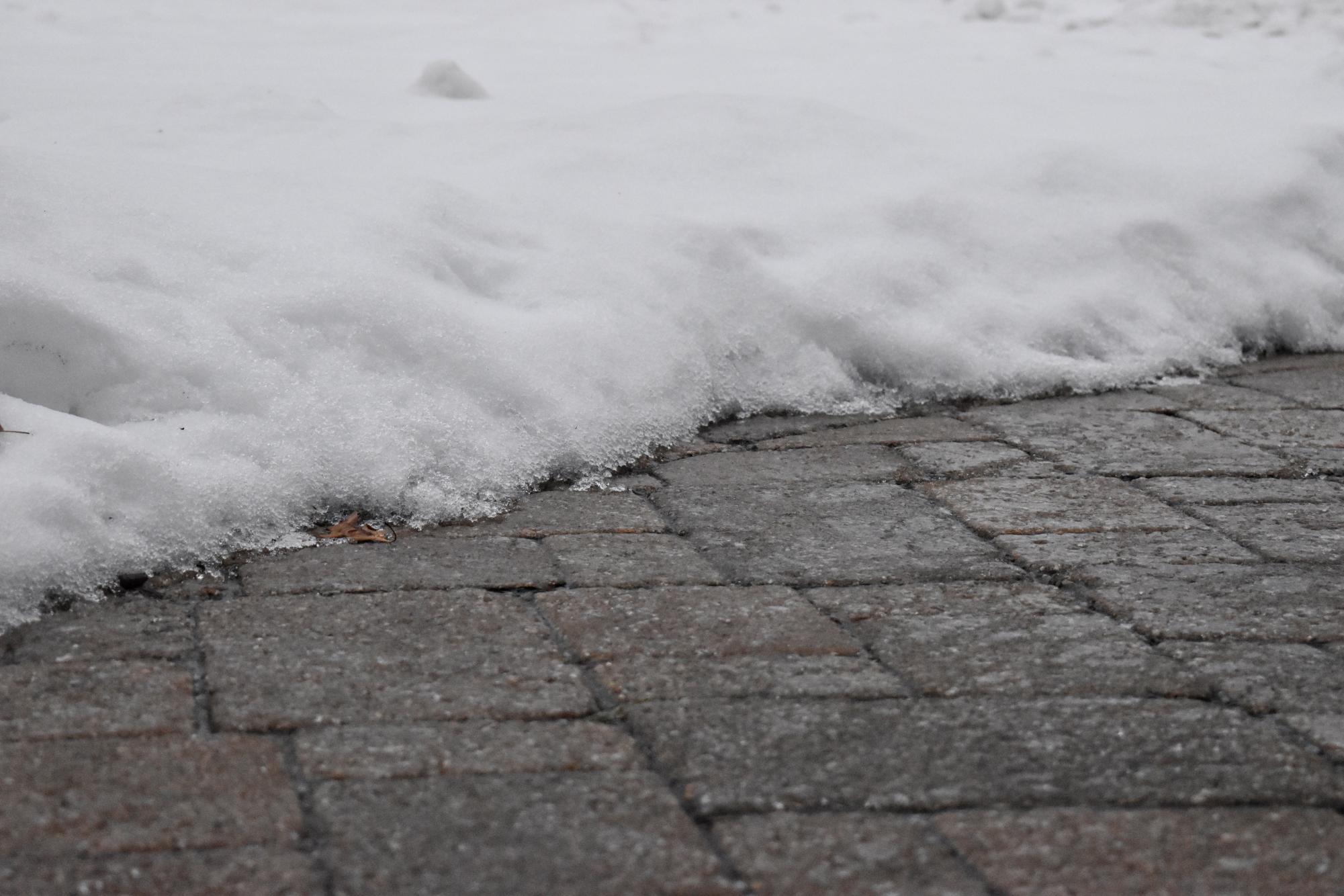 An ice layer has formed on top of the snow and all sidewalks and roads are covered in a layer of ice. 