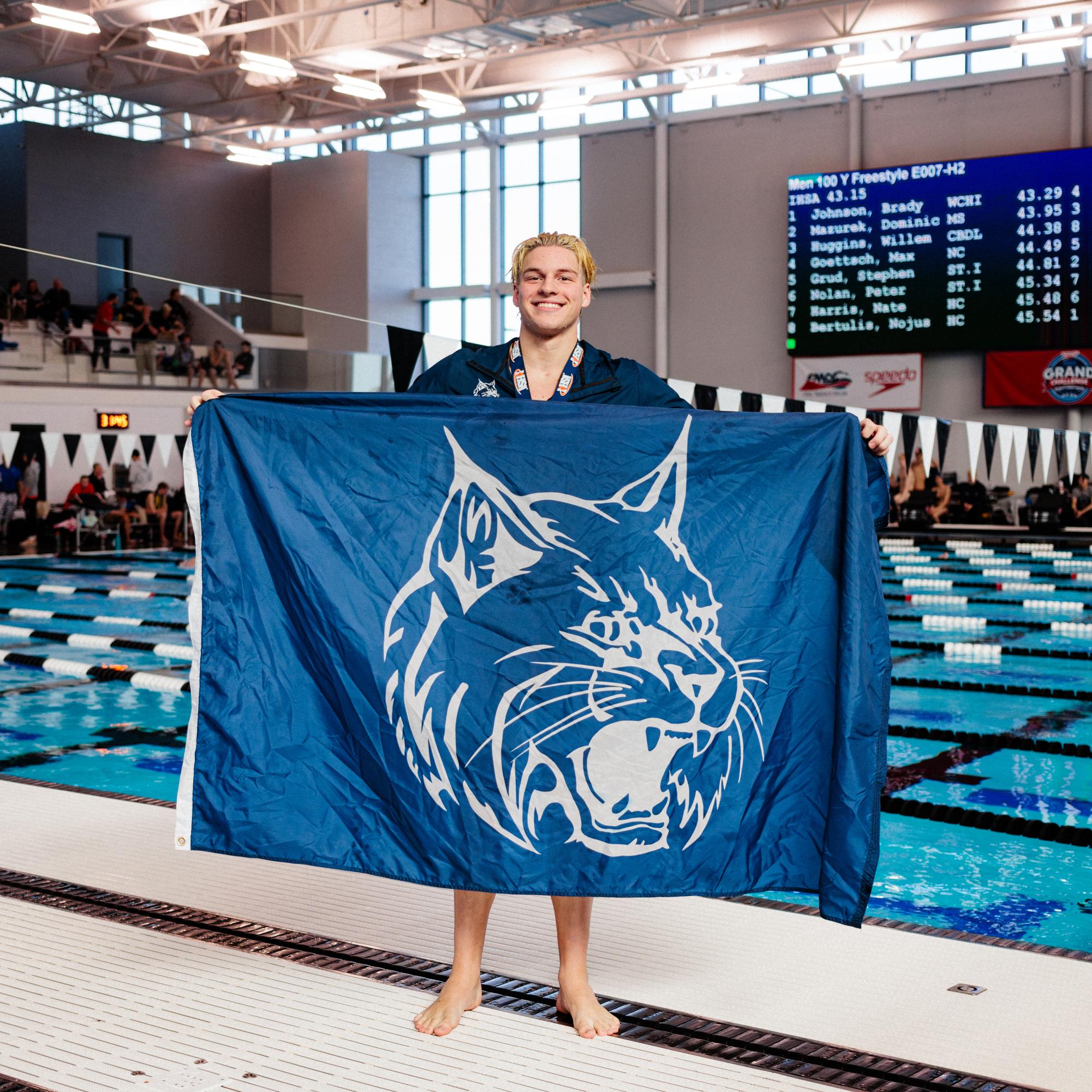 Senior Brady Johnson proudly unfurls a Wildcat flag in celebration of his first first-place finish of the day, clocking a 43.29 -only .14 shy of the state record he himself set just one day earlier- in the 100 free.