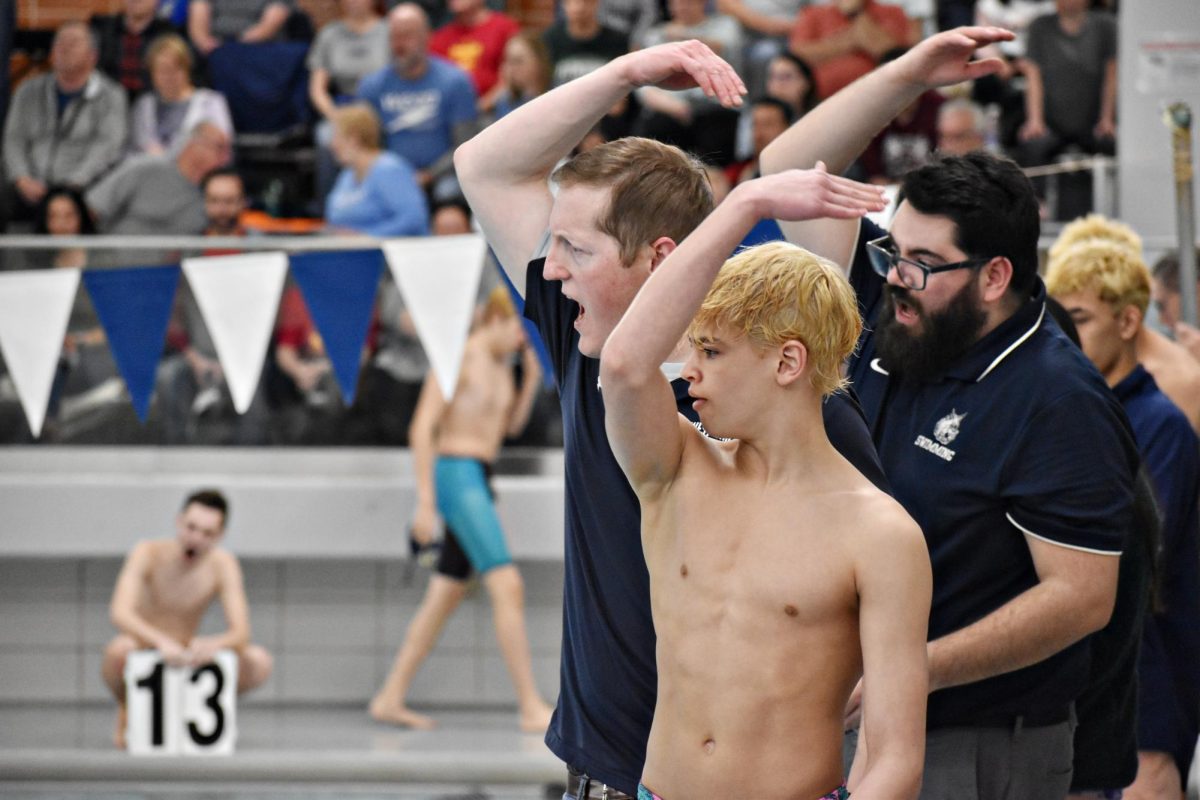 Coach Troy Murrary and Josh May, along with sophomore Logan Bremmner, wave their hands in encouragement for a swimmer.