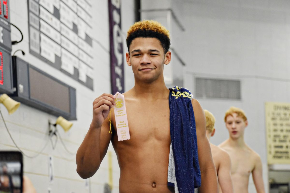 Sophmore Chris Davis, holds up his ribbon as swimmers from all schools are called to stand in recognition of their win in specific events.