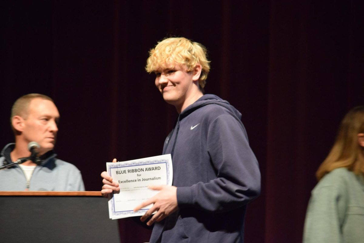 Senior Brandon Heath proudly looks at his peers while holding an award he contributed towards.