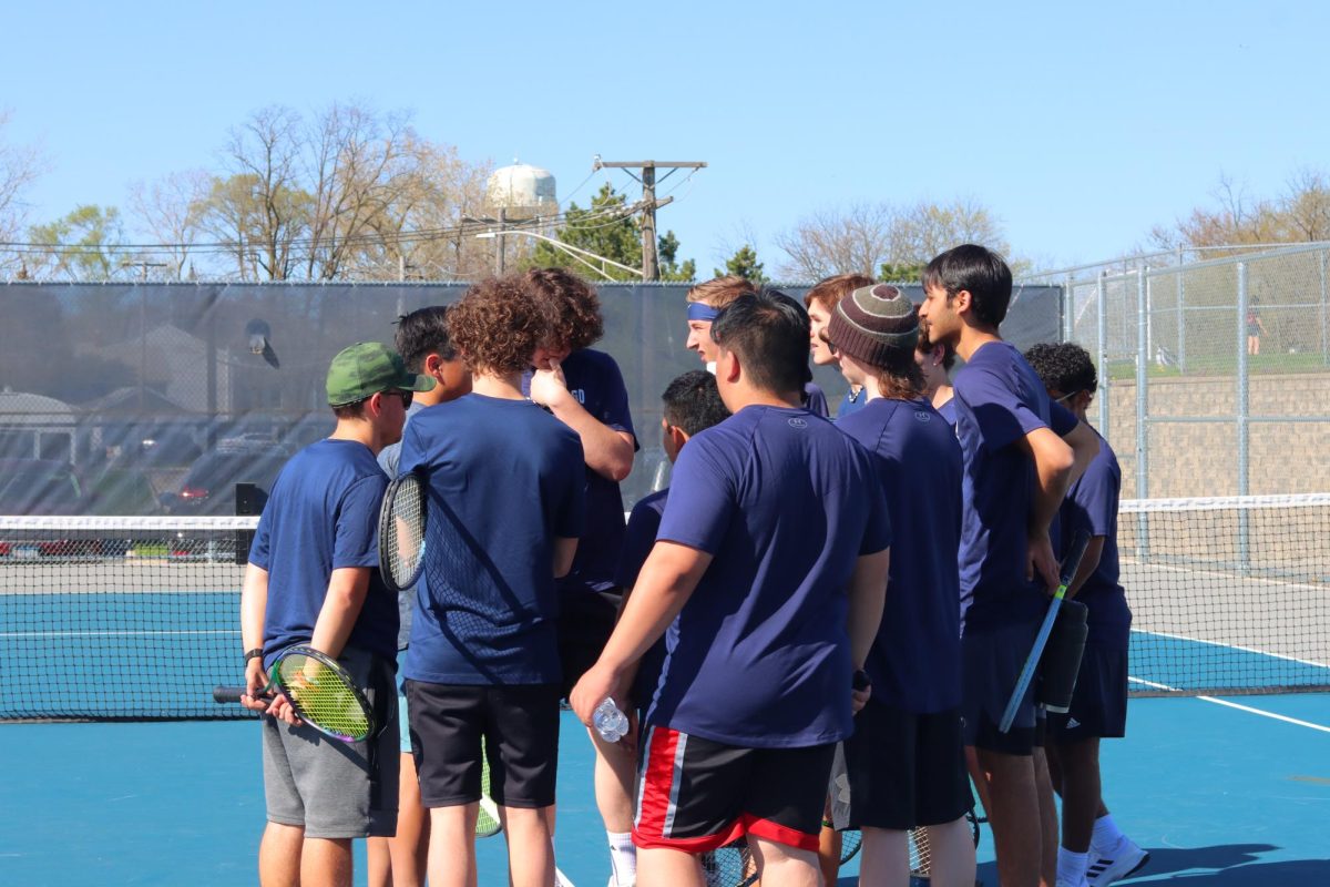 The Boys Tennis team huddles up to hear Coach Madden give a motivational speech before the game begins.