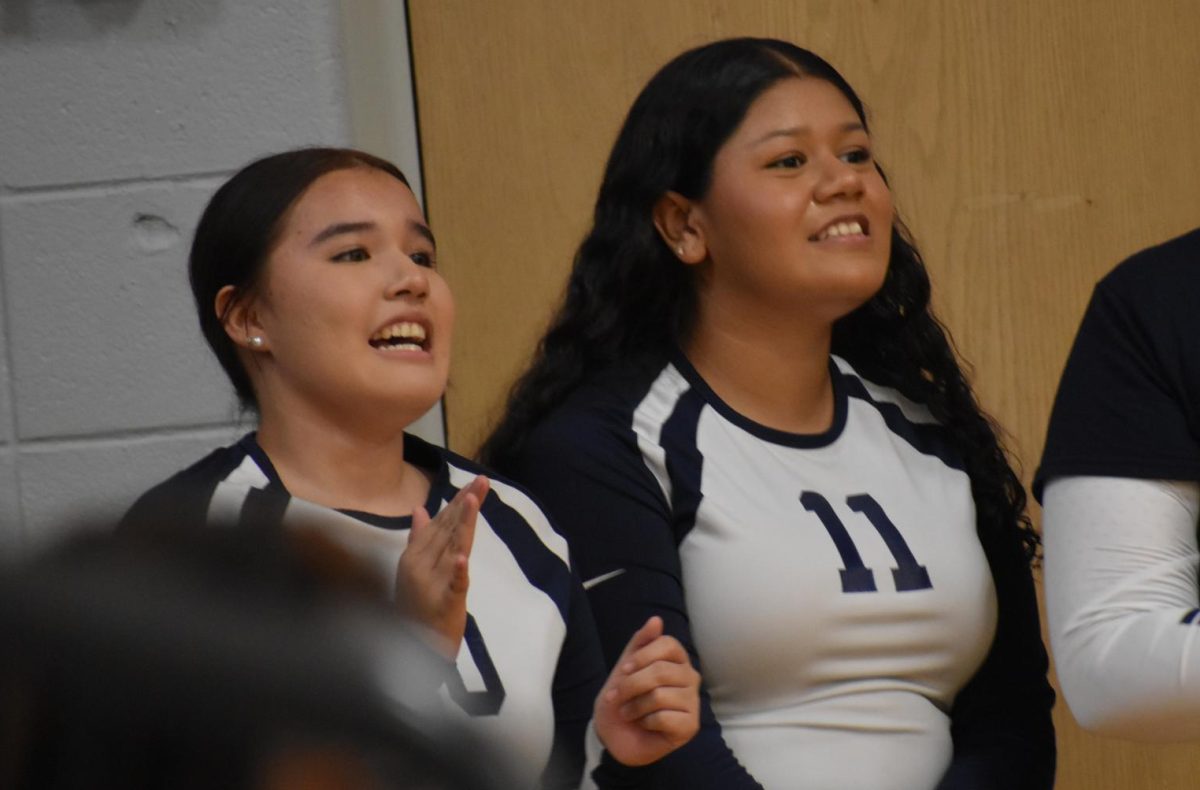 High school volleyball players cheer on the younger girls on the court. 