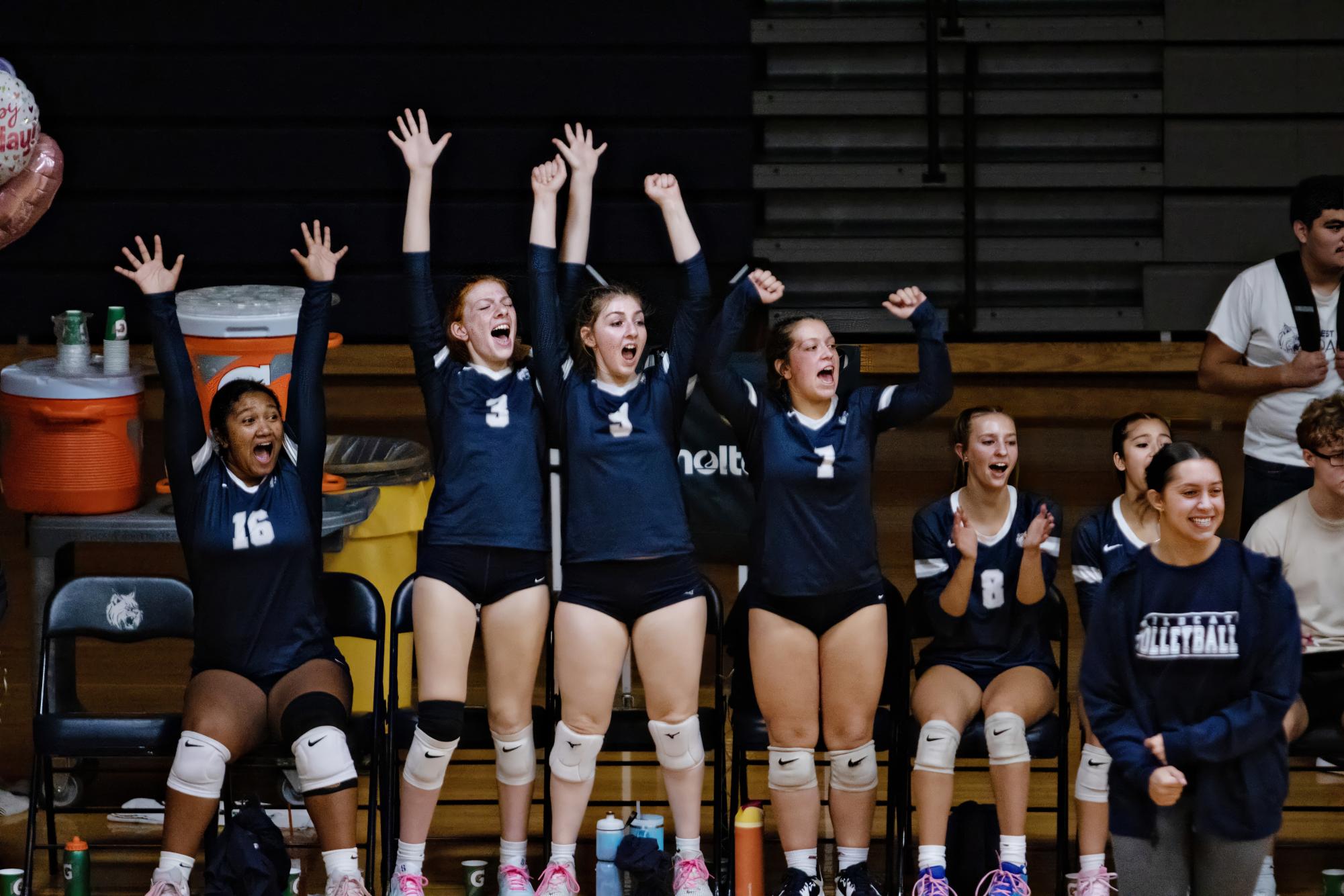 Varsity players cheer for those on the court as the volleyball team takes the lead in the game against Glenbard East. 