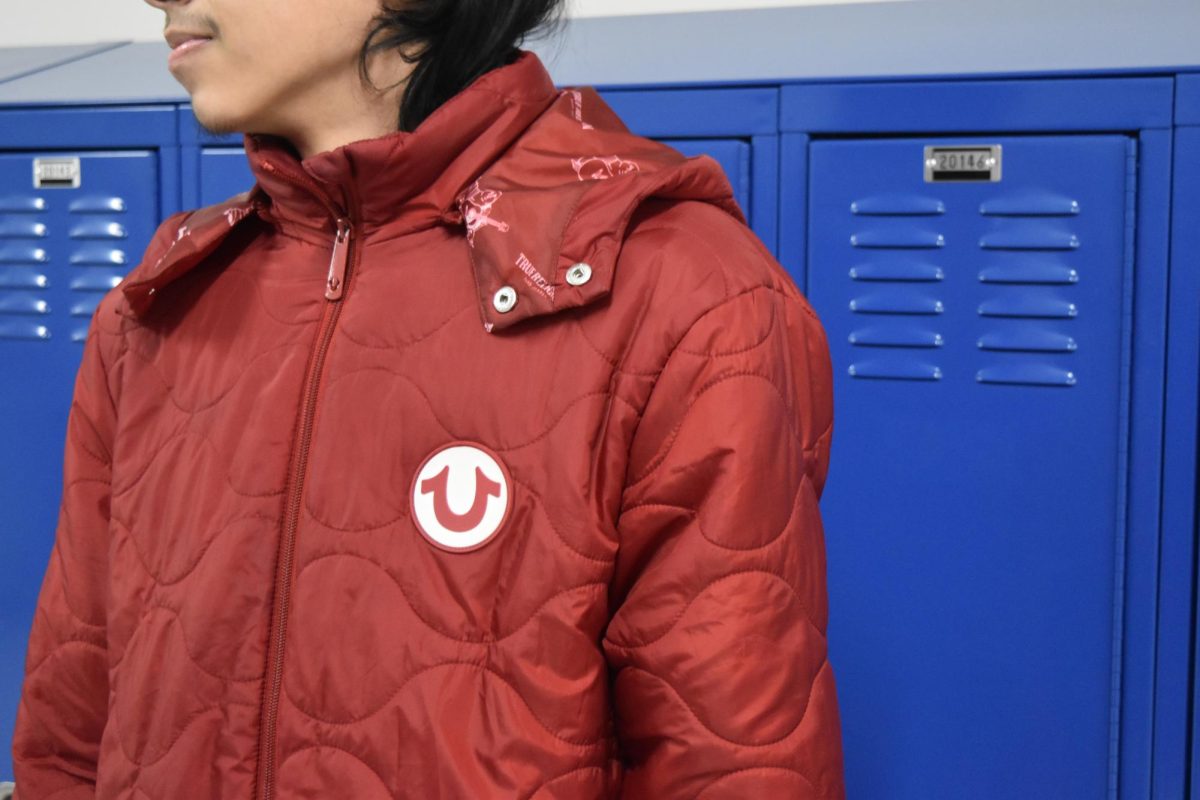 Junior Gumaro Correa models a red True Religion jacket at West Chicago Community High School during the winter months of 2025.