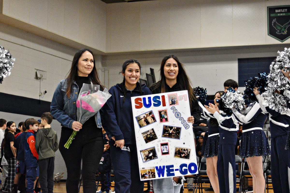 Susana Correa smiles alongside her family, holding a custom poster commemorating her wrestling journey during West Chicago’s Senior Night.