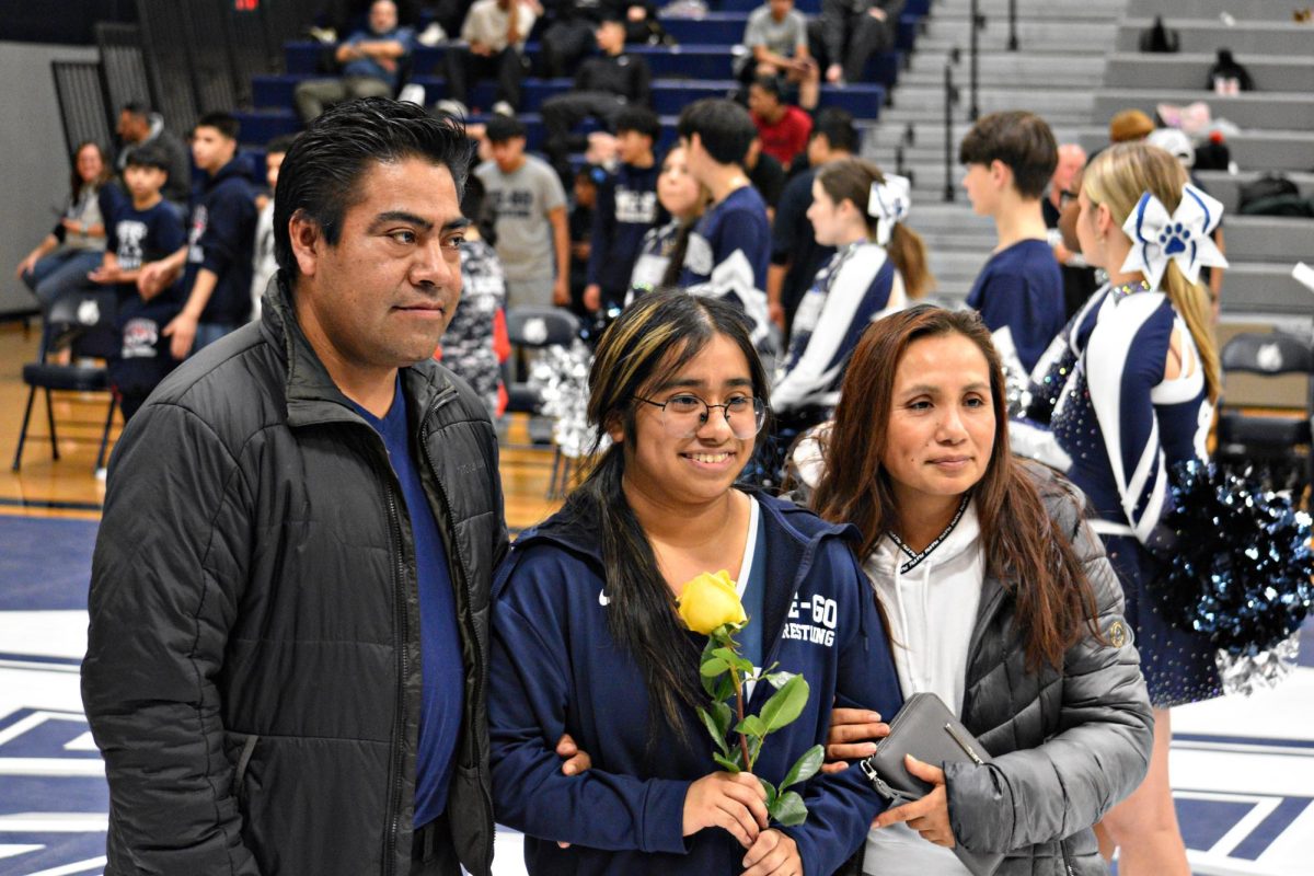 Pamela Cruz stands with her parents, holding a rose in recognition of her dedication to West Chicago wrestling during Senior Night.