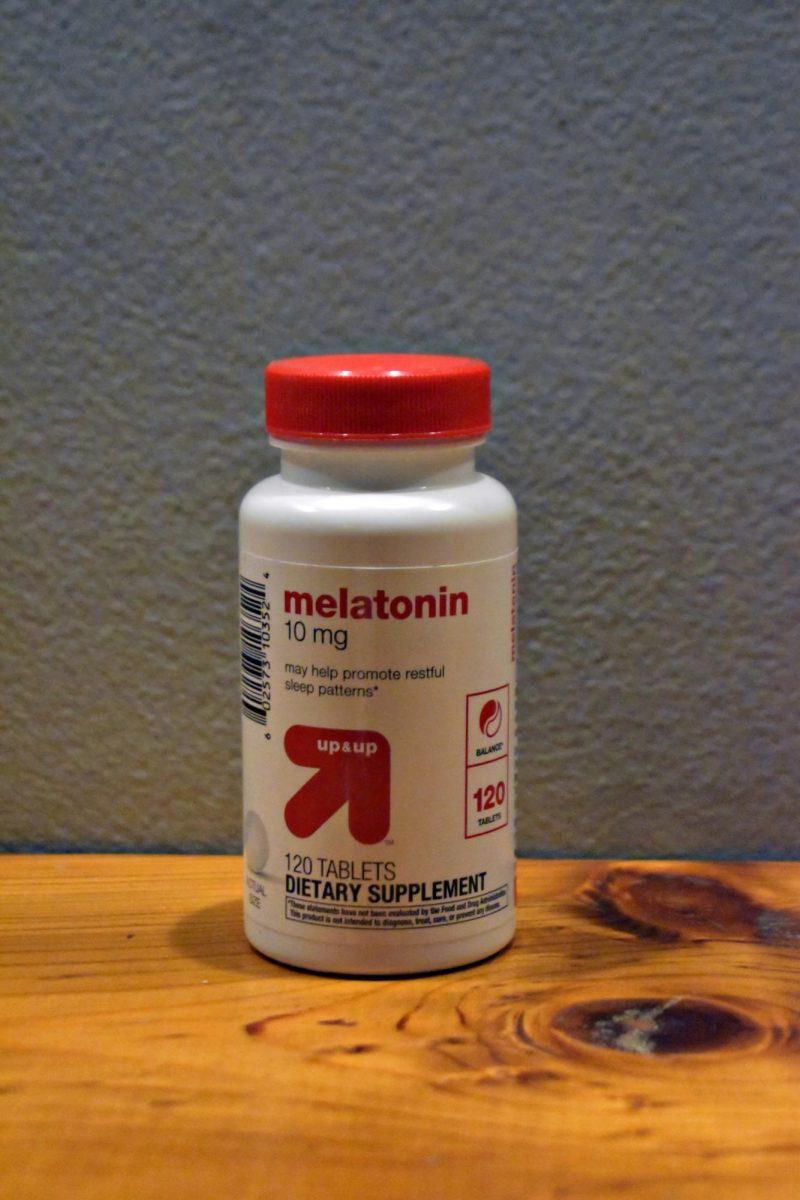 A bottle of melatonin supplements sits on a table, reflecting the growing use of sleep aids among teenagers and young adults despite emerging concerns about long-term health risks. (Image has been upscaled to improve quality)