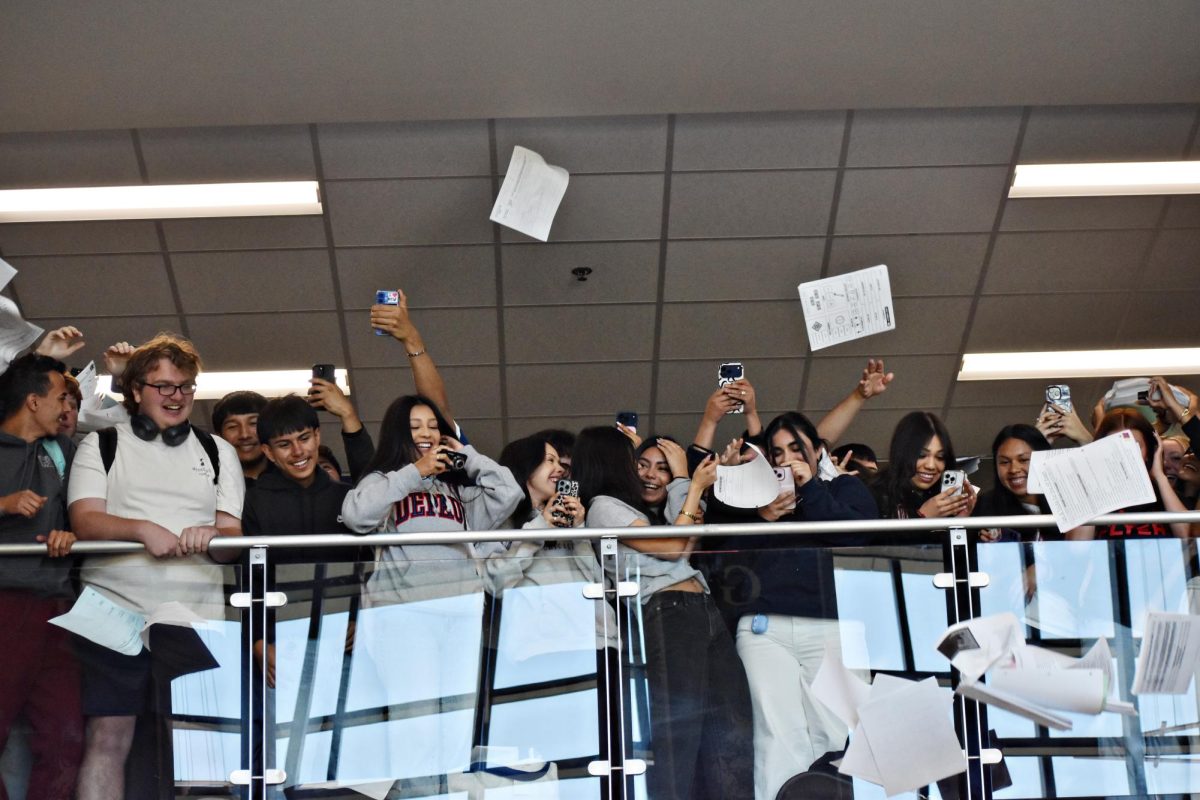 Papers continue to drift over the railing as seniors celebrate the final moments of the annual paper drop tradition at West Chicago Community High School. While many students had already emptied their folders and backpacks, others continued tossing assignments and notebooks into the air as classmates recorded the moment on their phones.